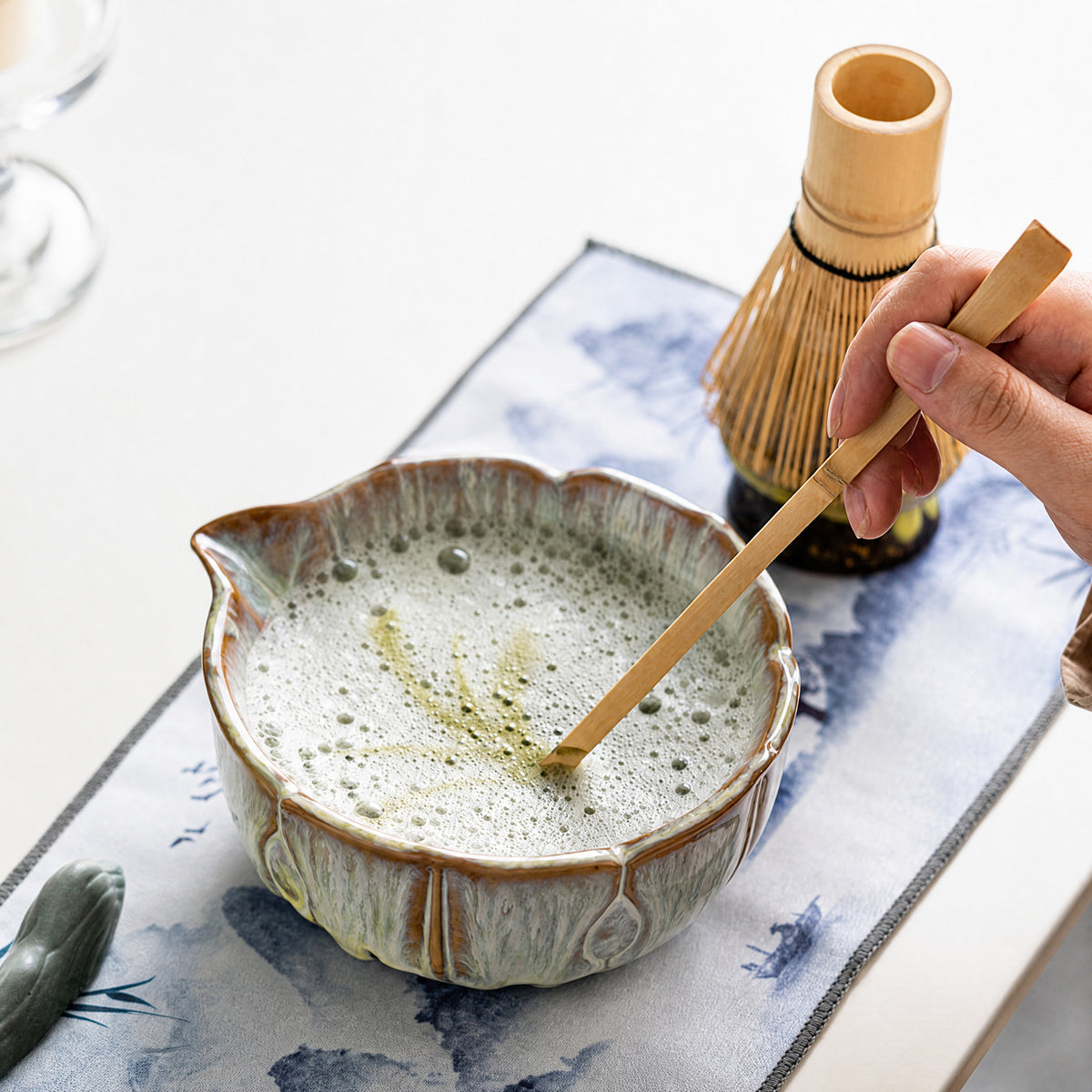 Hands whisking matcha with a bamboo chasen inside a kiln-glazed ceramic bowl