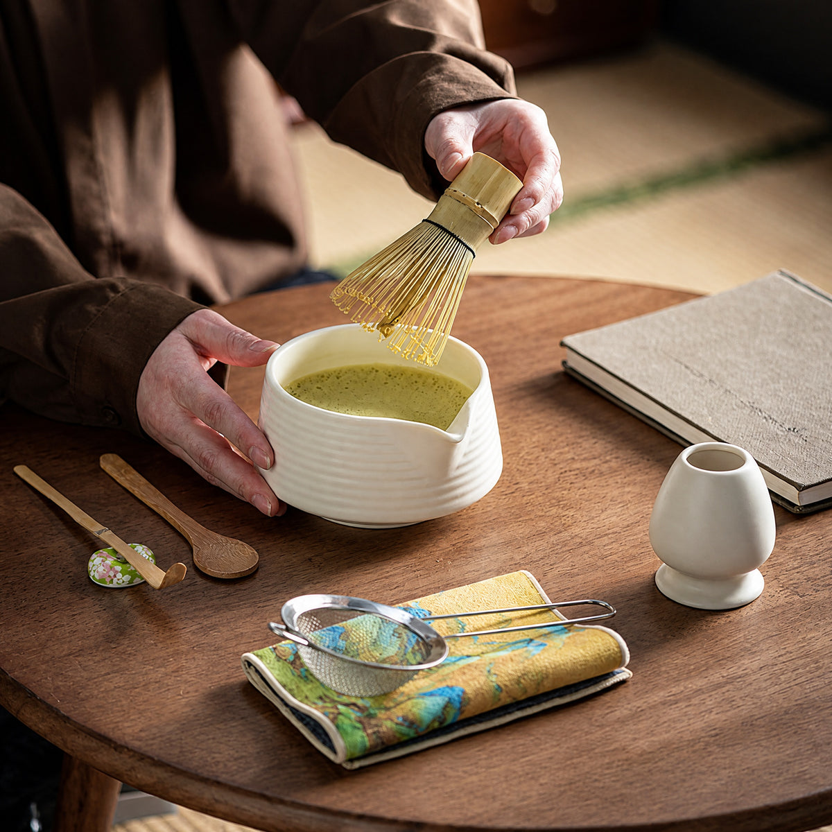 Matcha being prepared with a bamboo whisk in a ceramic bowl on a tea table