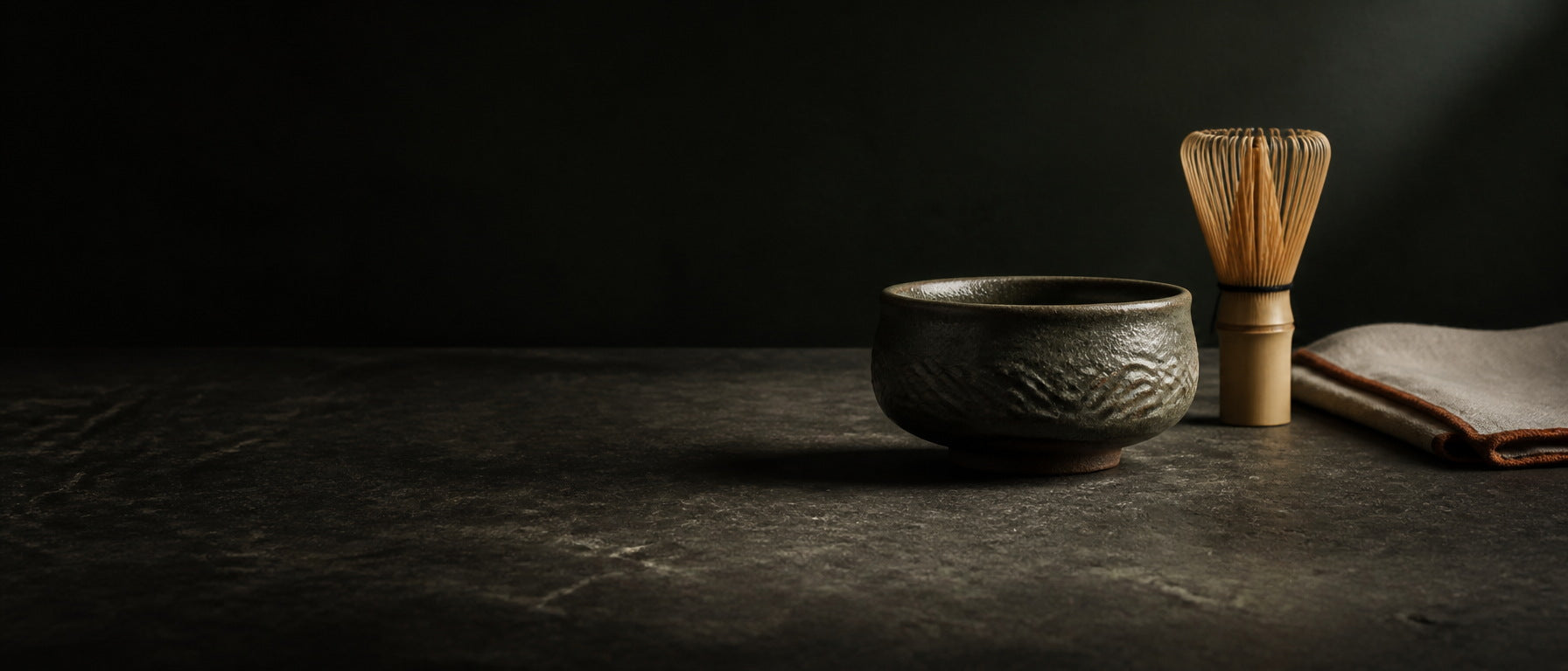 Glazed ceramic chawan and bamboo chasen on a stone surface